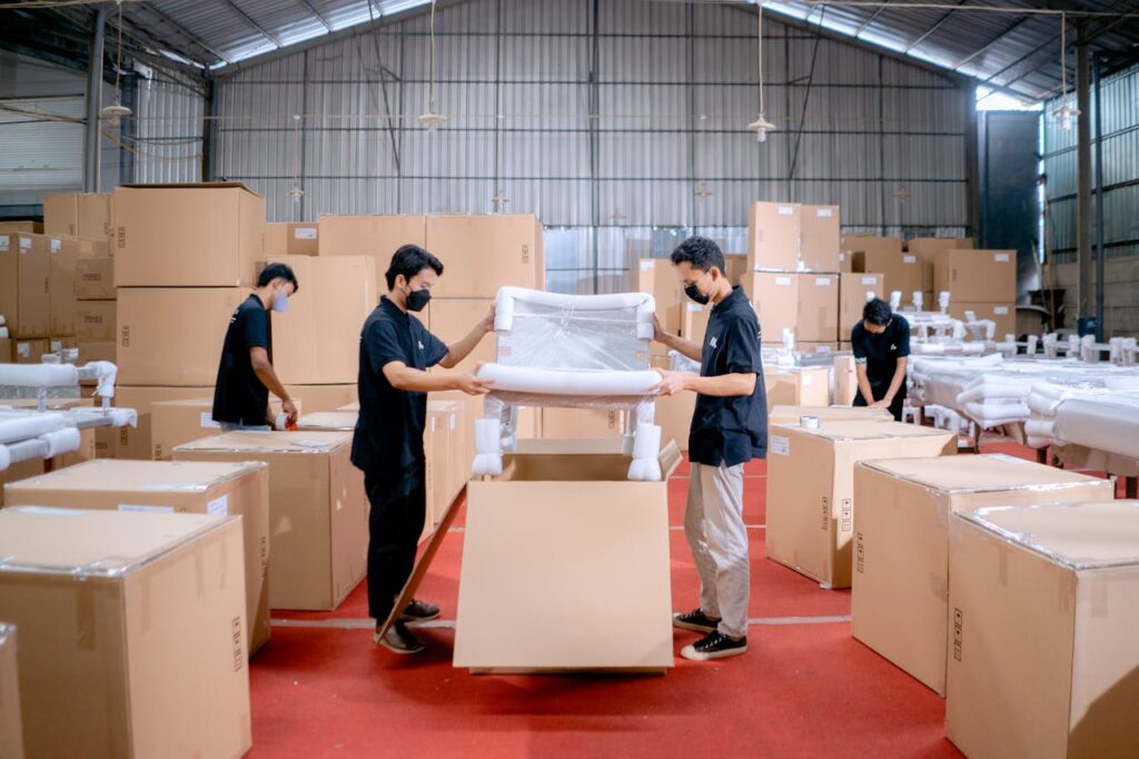 Men in a warehouse wearing masks, assembling and packing furniture into boxes with efficiency.