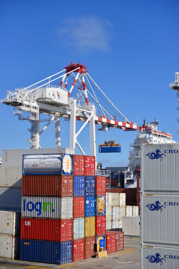 Colorful shipping containers stacked in a busy port with cranes overhead.